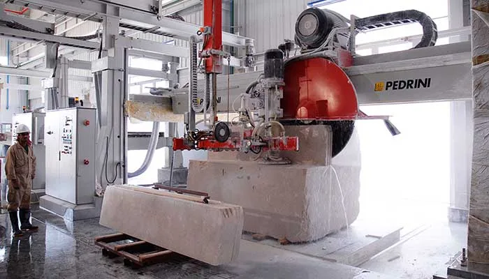 A Pedrini disc cutter opening a cream marble block, an operator alongside