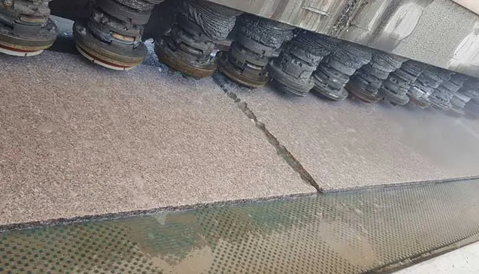 The row of polishing heads passing over a speckled granite slab