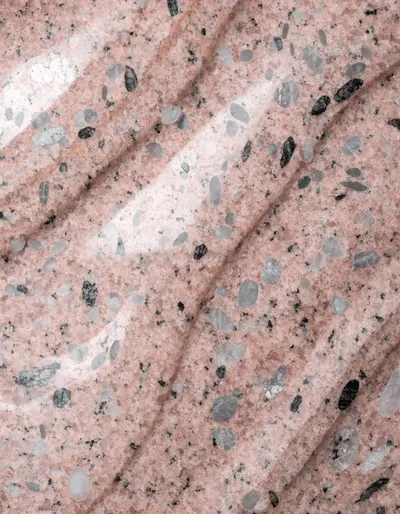 A polished slab of Rosa Nasr granite, a pale rose ground with gentle darker movement